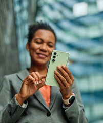 Portrait of a businesswoman woman using a smartphone mobile phone walking down the street, surrounded by moder corporate office buildings