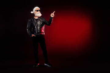 Rocky santa in leather jacket points forward in dark studio with red glow festive look christmas holiday themed fashion and lifestyle image