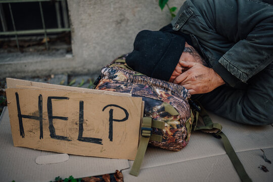 Homeless man sleeping on street with help sign