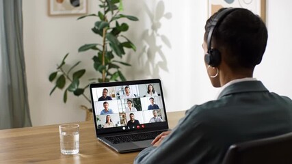 A professional individual of ambiguous gender in a modern home office with a sleek desk and vibrant plant, engaged in a virtual video call with diverse participants on a laptop, soft natural light,