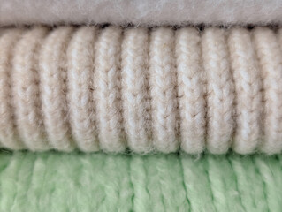close-up stack of rolled cozy fabrics: white, beige ribbed knit and pale green knit