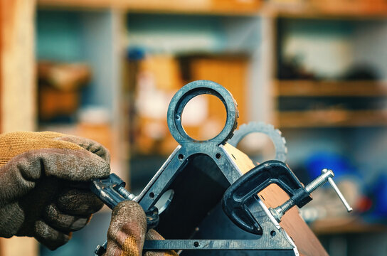 Male hands tighten metal parts together with clamp. Clamp has threaded screw. Industrial workshop.