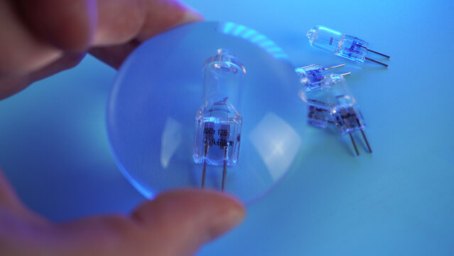 Capsule halogen lamp G4 under a glass magnifying lens, magnification of details. Several lamps on a blue background, subject shooting. - Powered by Adobe