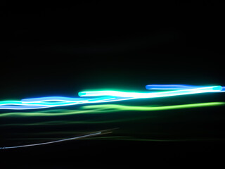 Elegant neon colored lines of light cut through the darkness of the night, giving a futuristic and dynamic impression of speed and movement, like a stunning digital abstract painting