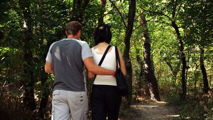 Happy couple walking along path at summer forest. Romantic pair going along trail at wild woodland....