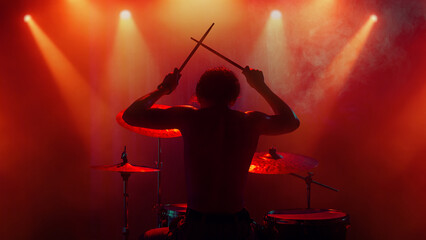 Fototapeta premium Drummer silhouette under orange light raising drumsticks in emotional finale. Concept of motivation, empowerment, creative advertising, music poster design, and inspirational stage art.