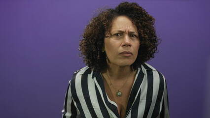Middle age hispanic woman raising fist in purple studio with serious expression; determination strength.