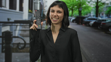 Woman holding remote control with finger pointing to remote on a city street; convenience empowerment joy.