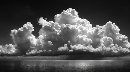 Dramatic monochrome cumulus clouds over a calm ocean horizon.