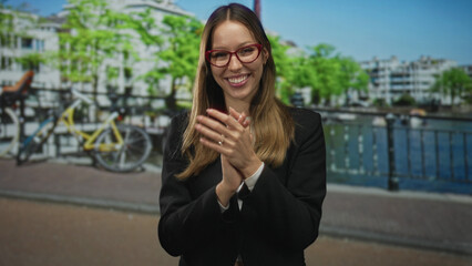 Woman clapping hands on a street in amsterdam beside a canal and parked bicycles, smiling and...