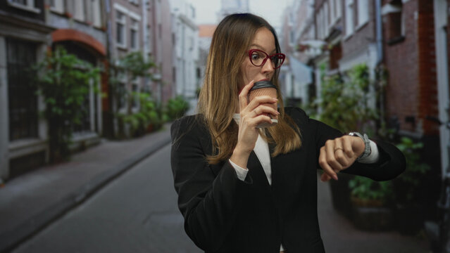 Woman holding takeaway coffee cup checking smartwatch while standing on narrow street with brick buildings and potted plants; morning commute hurry. - Powered by Adobe