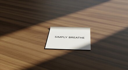 Gentle reminder "SIMPLY BREATHE" on a clean white card placed on a warm, textured wooden surface with soft sunlight casting a calming shadow, perfect for wellness and mindfulness inspiration.