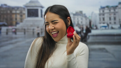 Woman smiling with engagement ring box in urban vatican setting, showcasing proposal moment...