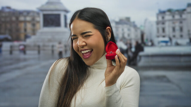 Woman smiling with engagement ring box in urban vatican setting, showcasing proposal moment outdoors with a joyful expression and iconic architecture in the backdrop. - Powered by Adobe