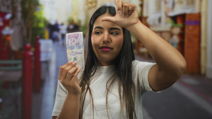 Woman holds tattered pesos while gesturing disdain on a crowded street with a young latin hispanic...
