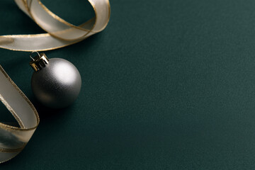 Elegant holiday card design featuring a silver ornament on a deep forest green background with a gold ribbon