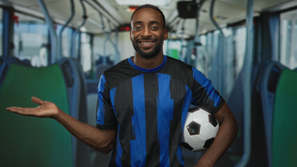 Man holding soccer ball giving thumbs up inside bus on street, wearing blue black striped jersey and smiling  team pride. © Krakenimages.com