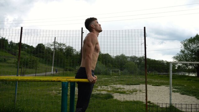 Young sportsman doing push ups on parallel bars at nature. Strong sporty man exercising at sports ground. Male shirtless athlete training hard outdoor. Concept of active sportive lifestyle. Slow mo