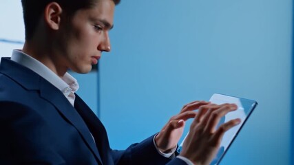 Man in a suit interacts with a futuristic transparent tablet, navigating digital data on a blue background in a modern, technology-driven world. - Powered by Adobe