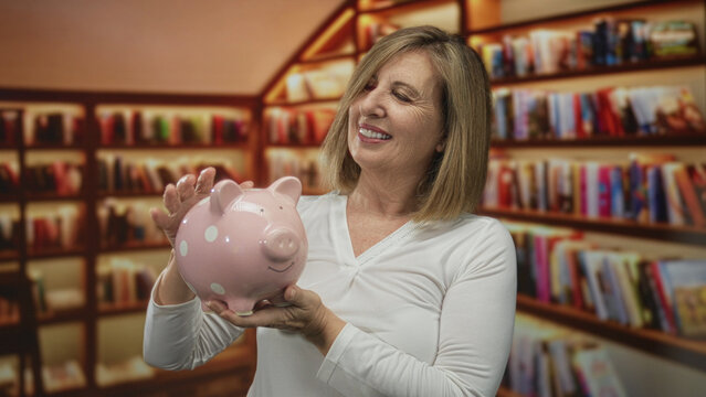 Middle aged woman holds pink piggybank with bare hands in building lined with bookshelves; financial security contentment.