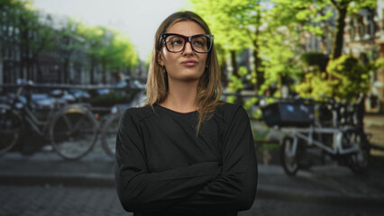 Fototapeta premium Woman wearing oversized glasses with arms crossed and pursed lips on street in amsterdam canal district; skepticism irony.