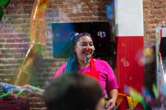 Mujer payaso sonriendo entre burbujas de jab&oacute;n en una fiesta