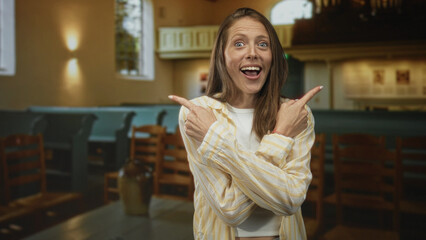 Woman pointing both fingers and shrugging with bare hands amid wooden pews in church building, open...