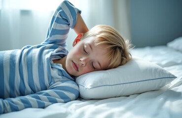 Blond boy wearing blue striped pajamas sleeps peacefully on a white pillow and bedsheets. His arm is bent behind his head. He appears relaxed and content in his sleep.