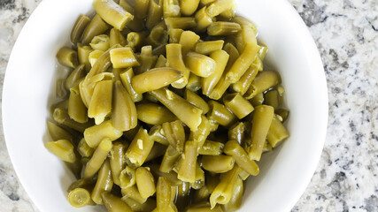 Fresh canned green beans in a white bowl on a marble countertop with a healthy appearance