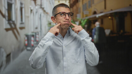 Man wearing glasses stands playfully in a quaint street surrounded by european architecture, embracing a lighthearted outdoor moment.