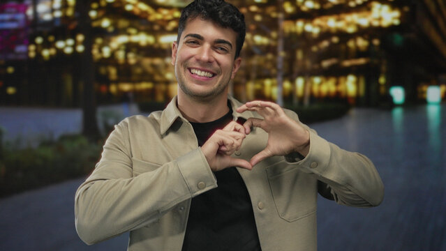 Man forms heart shape with hands at downtown plaza; love affection happiness joy. - Powered by Adobe