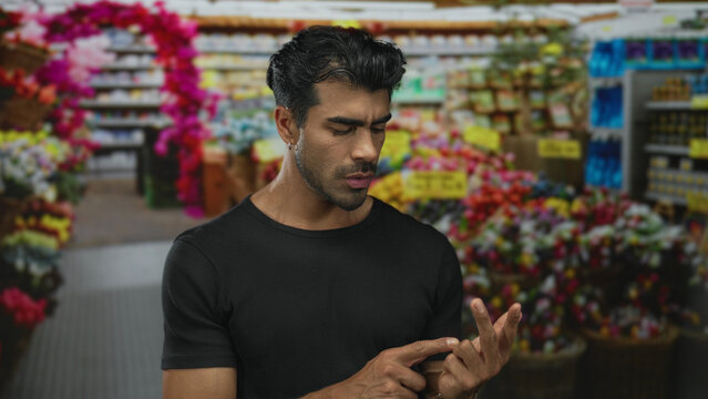 Young hispanic man counting fingers in street flower shop aisle amidst vibrant blossoms; uncertainty.