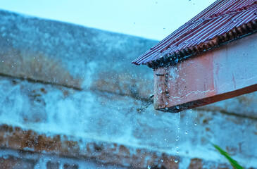 Close-up view of vibrant raindrops splashing off a building's corrugated metal roof during a monsoon in India, creating a dynamic weather scene.