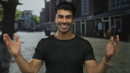 Fototapeta premium Young hispanic man grinning while raising open palms wide to show a large gap on street wearing a black shirt; confidence.