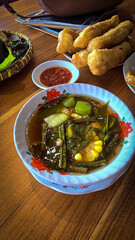 Mixed vegetable tamarind called sayur asem featuring leafy greens, corn, and potato pieces in a rich broth. Cozy, wholesome meal set on a wooden table