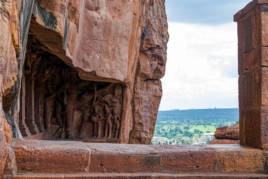 Ancient rock-cut temple carvings are framed by the cave entrance at Badami, Karnataka, India, revealing a scenic distant landscape. This historic site showcases incredible ancient architecture. - Powered by Adobe