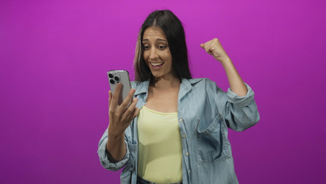 Woman pointing to smartphone in studio with vivid purple backdrop and casual denim shirt; curiosity. - Powered by Adobe