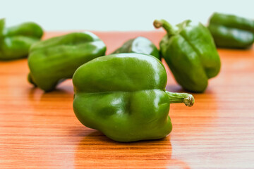 A close-up, vibrant shot of fresh green bell peppers on a light wooden surface in India, highlighting healthy eating.