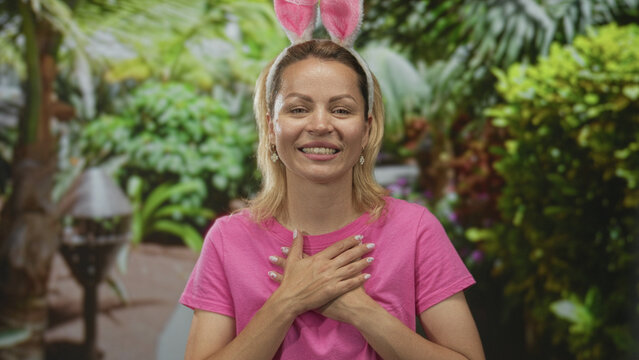 Woman wearing pink shirt smiling and clutching chest in the lush green park; gratitude sincerity warmth.
