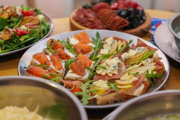 Olivier salad, sandwiches, canapés, bruschetta. A Christmas scene with meat delicacies against a dark wood background. An assortment of cheese and meat appetizers.