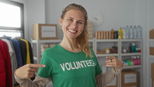 Woman wearing a green shirt is pointing inside a warehouse where a blonde young volunteer is smiling with crossed arms for a charity event.