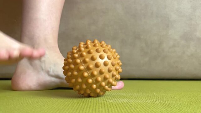 White woman doing foot massage on spiky massage ball for massage and training. Rehabilitation exercises. Home workout.
