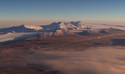 Majestic snow-capped mountains rise above a vast, arid landscape under a clear sky with a layer of fog at the base