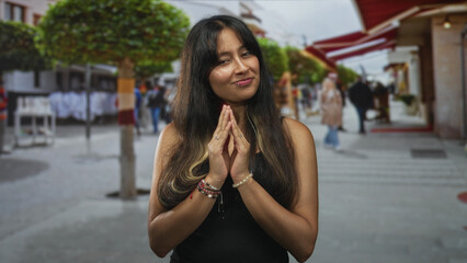 Woman with hands pressed together in prayer on downtown street wearing bracelets and rings; quiet gratitude.