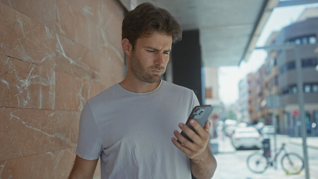 Man holding smartphone with hand on chin on street near parked bicycle and cars, looking at screen; thinking uncertainty doubt.