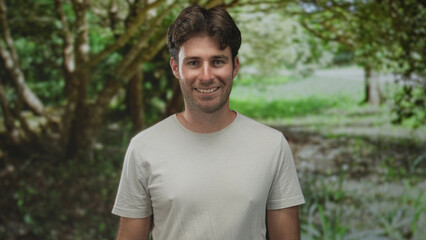 Man smiling with face visible and relaxed posture in a green park forest setting; serenity friendly.