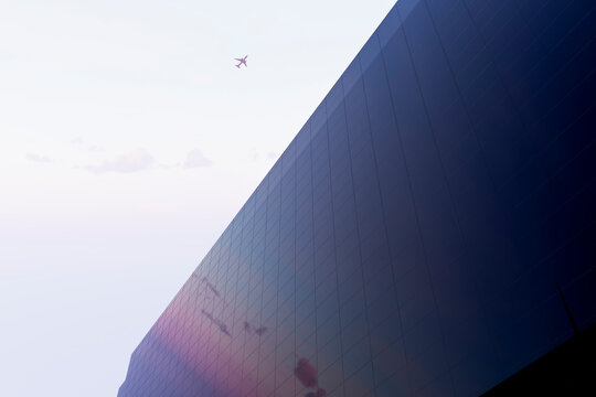 Airplane over 3D mirrored skyscraper in morning sky