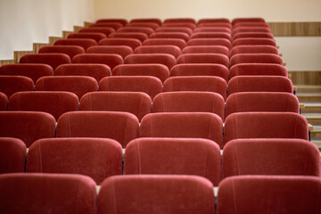 Fototapeta premium A close-up, front-on view of the empty maroon seats in a university lecture hall. The soft, upholstered chairs are arranged in neat rows, with wooden steps visible on the side.