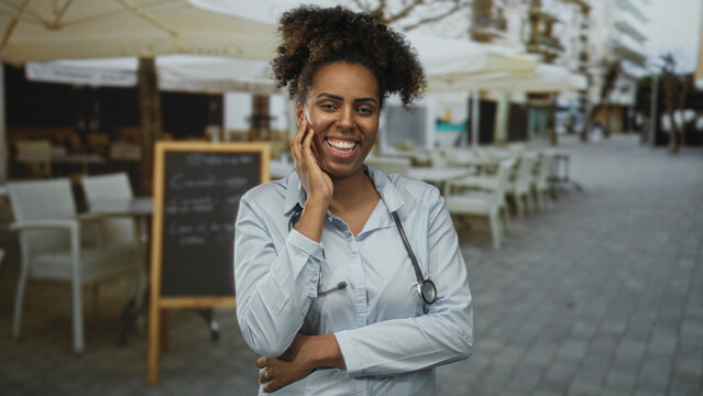 Woman doctor with stethoscope, hand on cheek and broad smile on a street terrace; confidence and care.