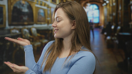 Woman in blue sweater holds open palms toward gilded paintings in ornate gallery hall of museum building; curiosity.